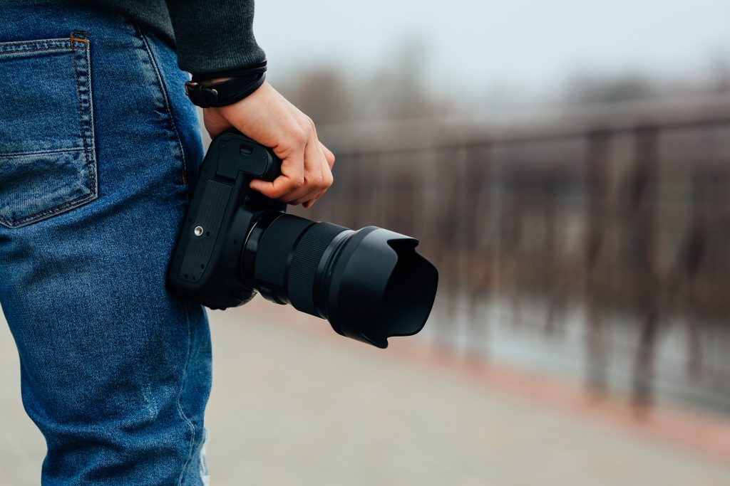 Close-up view of male hand holding the professional camera on the street. Dressed in jeans.